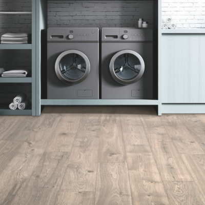 A tidy laundry room with light laminate flooring, gray front-loading washing machines, and blue-green cabinets with neatly arranged towels.